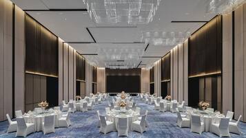 A spacious banquet hall with round tables, white chairs, and a blue carpet.