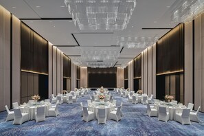 A spacious banquet hall with round tables, white chairs, and a blue carpet. - Crowne Plaza Shangluo (Shanglou)