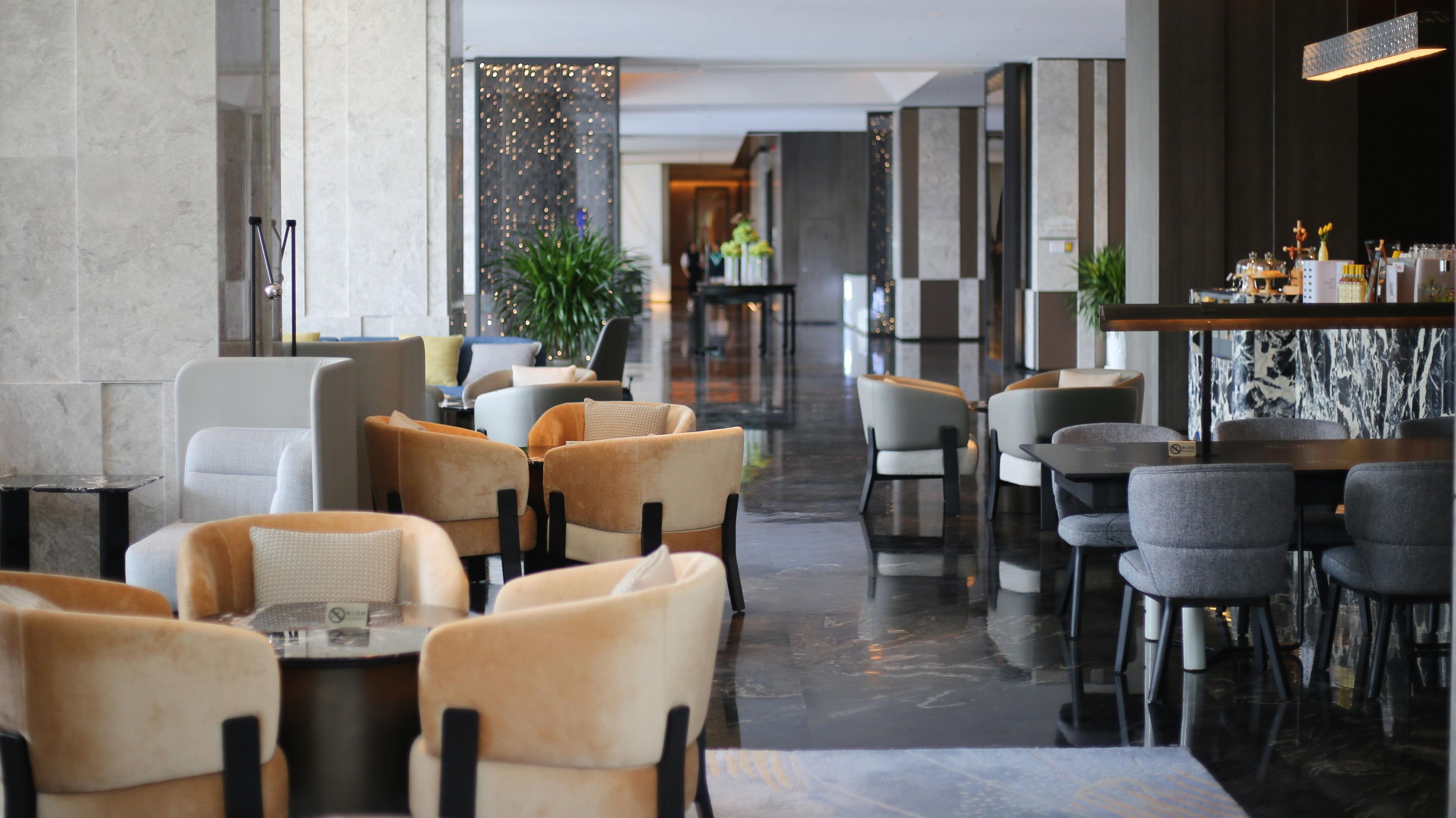 A modern hotel lobby with a mix of seating areas, including sofas and chairs, arranged around a central walkway.