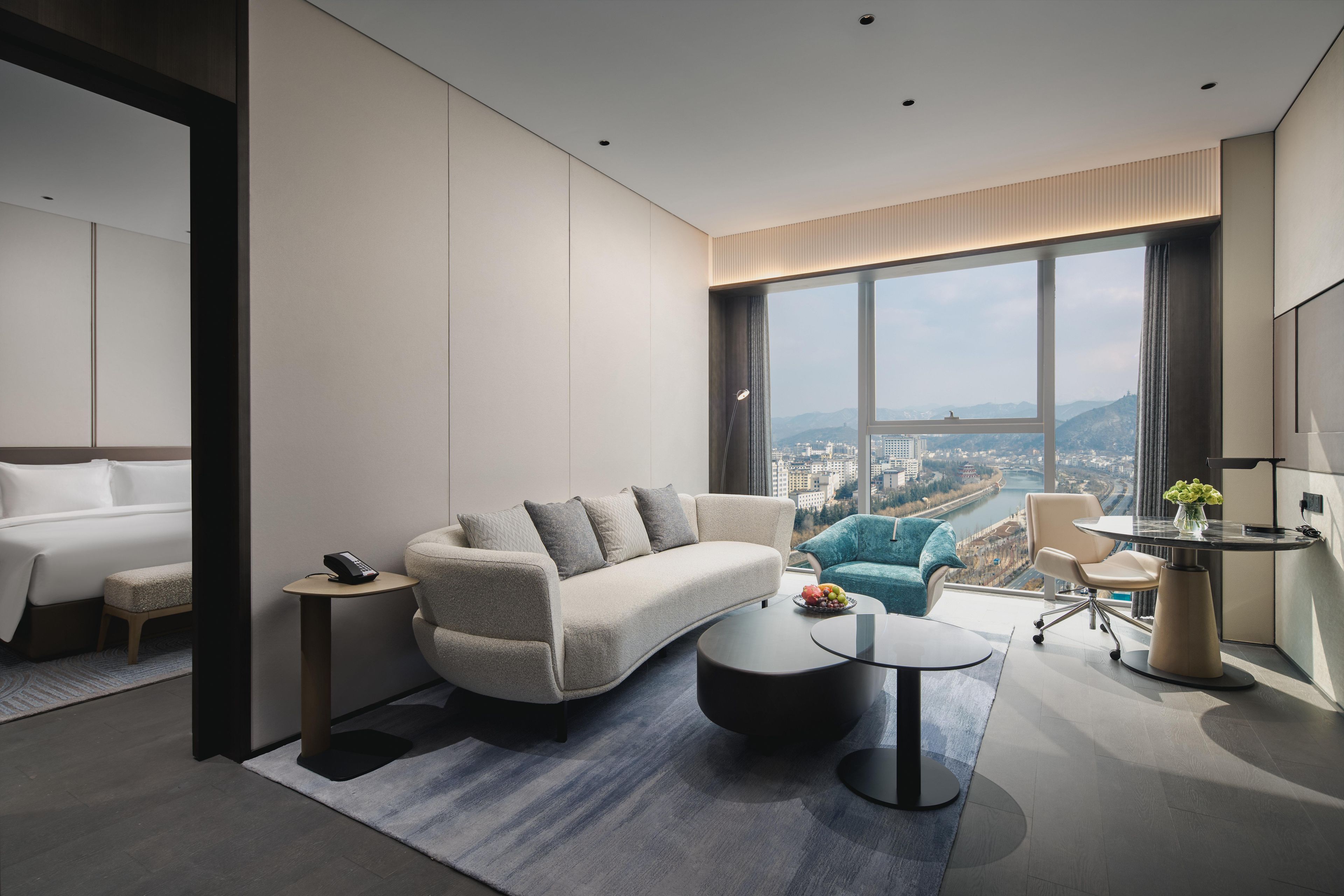Une chambre d’hôtel moderne dotée d’une grande fenêtre, d’un canapé, d’un bureau et d’un lit.