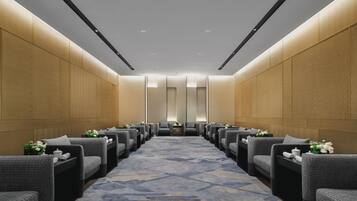 A hotel room with a long corridor, grey upholstered chairs, a patterned carpet, and wooden panel walls.