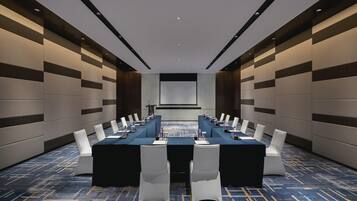 A conference room with a long table, white chairs, and a projector screen.