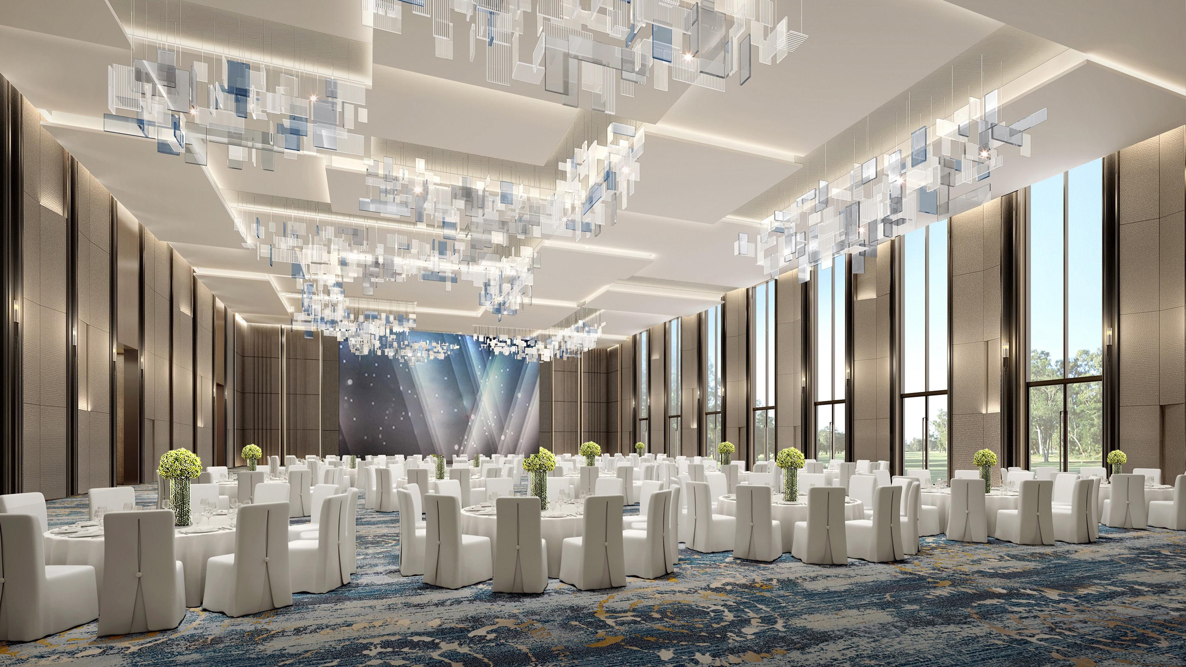 A spacious conference room with a high ceiling, modern chandeliers, and large windows offering a view of the outdoors.