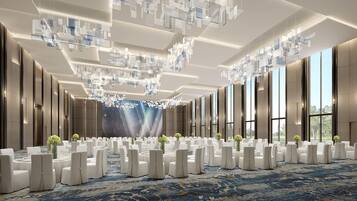 A spacious conference room with a high ceiling, modern chandeliers, and large windows offering a view of the outdoors.