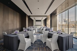 Un salón de conferencias con mesas y sillas, ventanas amplias y vistas a la ciudad.