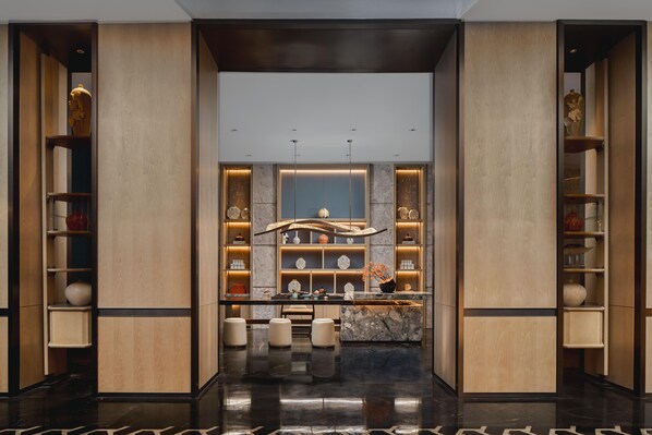 A modern hotel lobby with a central reception desk, marble flooring, and wooden paneling. - Crowne Plaza Shangluo (Shanglou)