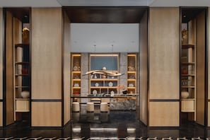 A modern hotel lobby with a central reception desk, marble flooring, and wooden paneling.
