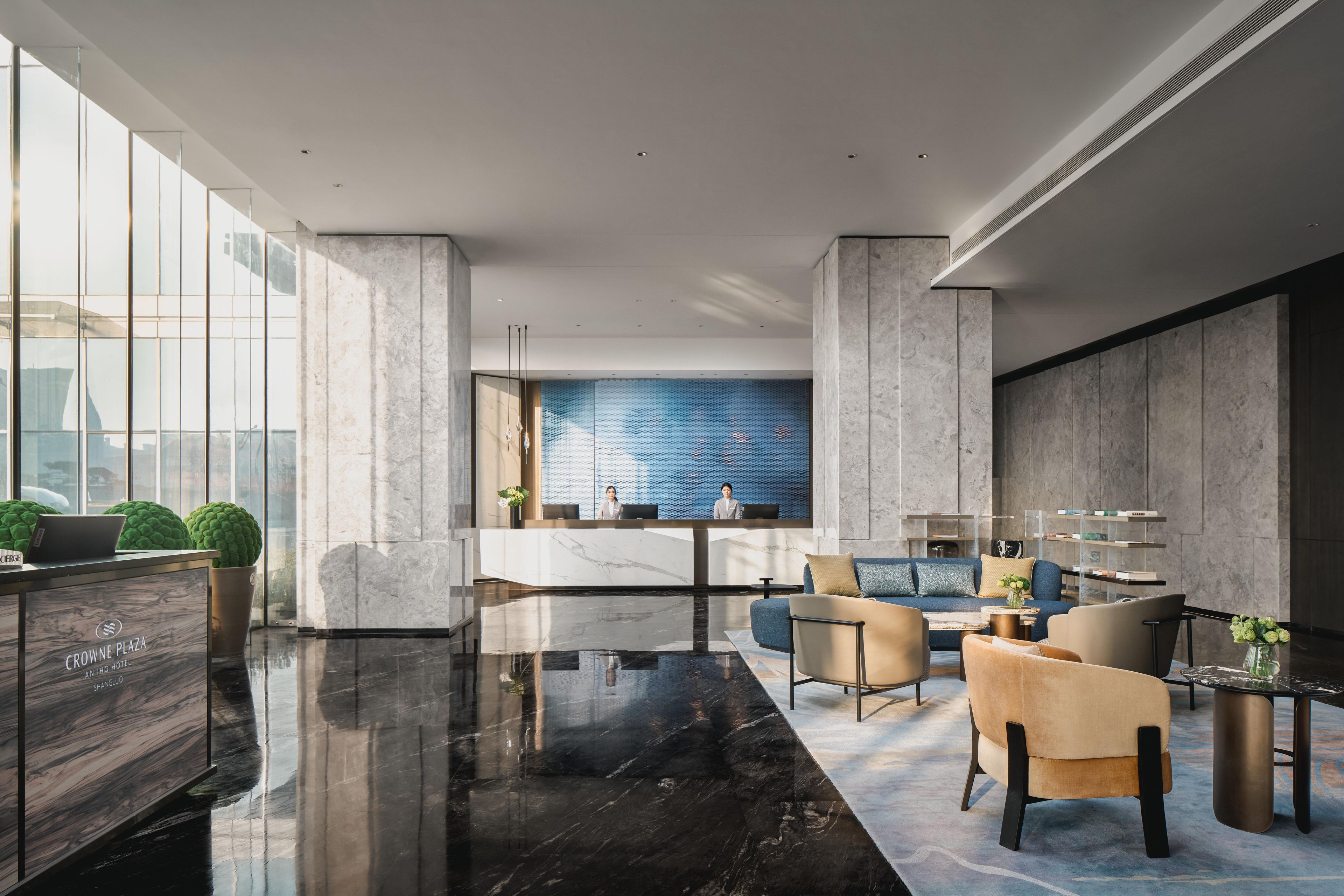 A modern lobby with a marble reception desk, seating area with sofas, and a large window offering a city view.