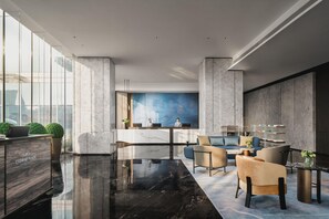 A modern lobby with a marble reception desk, seating area with sofas, and a large window offering a city view.