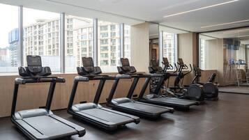 A gym with treadmills, elliptical machines, and stationary bikes arranged in rows.