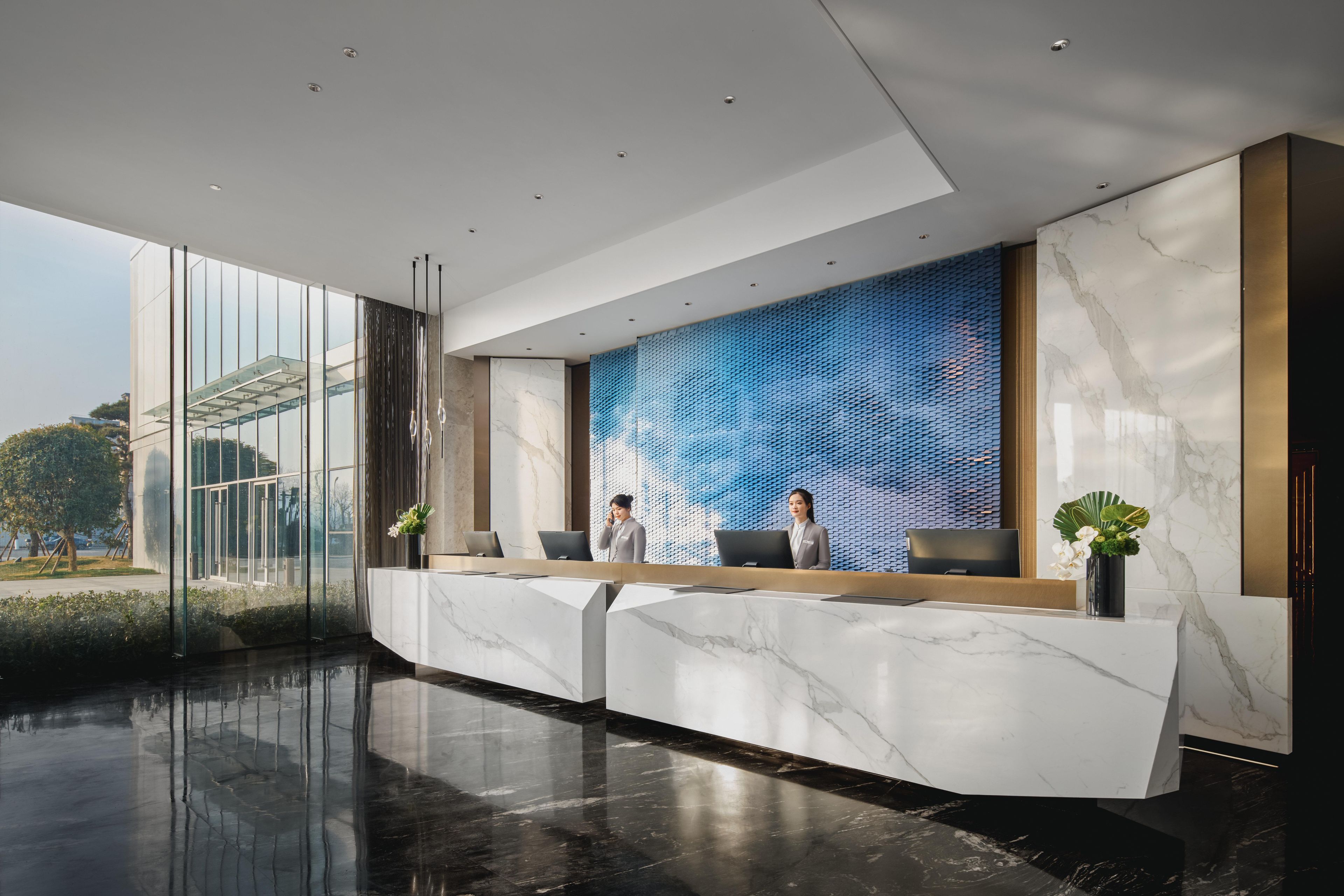 A modern reception area with a marble reception desk, two receptionists, and a large digital display wall.