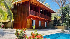 A wooden house with a balcony, a swimming pool, and potted plants. - Charming lodge in beautiful Playa Samara with WiFi (Playa Samara Guanacaste Province)