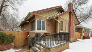 A two-story house with a brick chimney, a front porch with a black railing, and a wooden fence. - Colorado Bay A (Colorado Springs)