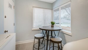 A corner room with a round table and two stools, a window with blinds, and a door with a handle. - Colorado Bay A (Colorado Springs)