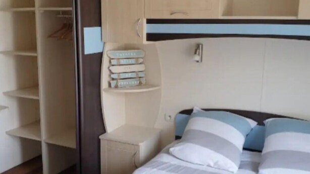 A bedroom with a bed, a wardrobe, and a shelf unit. - Mobilhome Ty Fregamano, Terrain Privé, vue mer (Locquirec)