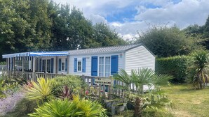A white building with blue shutters and a striped awning, surrounded by lush greenery and a sign reading 'FREGANNO'. - Mobilhome Ty Fregamano, Terrain Privé, vue mer (Locquirec)