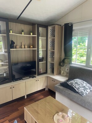 Una sala de estar moderna con una televisión de pantalla plana, estantes de madera, un sofá gris y una mesa de centro de madera.