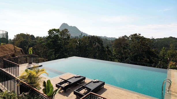 An infinity pool with lounge chairs, surrounded by lush greenery and a mountain in the background. - Morickap Lord's 83, Trademark Collection by Wyndham (Sulthan Bathery)