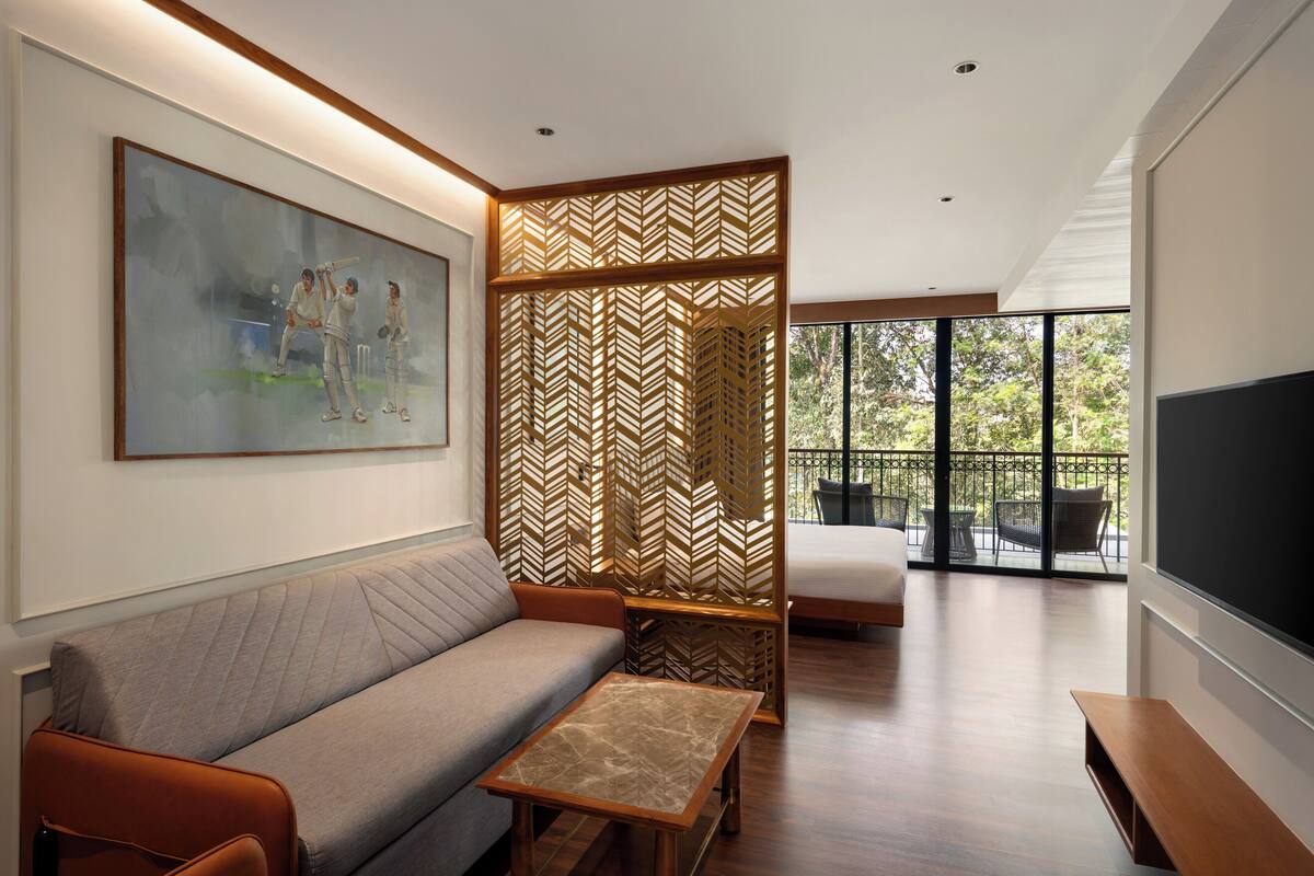 A modern living room with a sofa, a coffee table, a large painting, and a balcony with outdoor furniture.