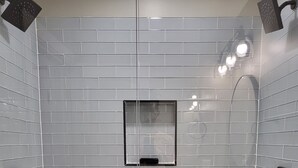 A shower area with gray hexagonal tiles, a black towel bar, and a small mirror on the wall.