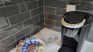 Máquina de café e um prato com cápsulas de café e saquinhos de adoçante em uma bancada de cozinha.