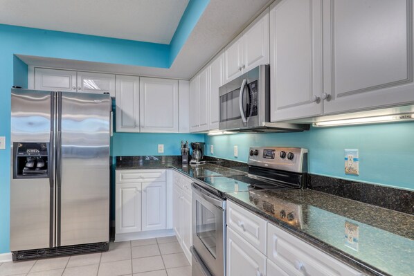 A modern kitchen with white cabinets, stainless steel appliances, and a blue accent wall. - Vibrant Beachy Condo! Barefoot Landing Resort! Yacht Club Villa by the Beach! (North Myrtle Beach)