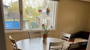 A dining area with a round table and four chairs, a potted plant, and a window with a view of trees and a building. - Charming 2 bedroom home.🏔 (Cranbrook)