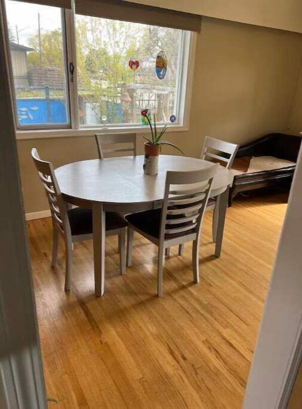 A dining area with a round table and four chairs, a potted plant, and a window with a view of trees and a building. - Charming 2 bedroom home.🏔 (Cranbrook)