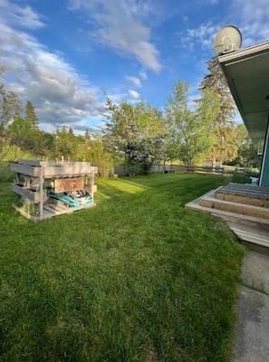 A well-maintained backyard with a wooden deck, a satellite dish, and a variety of trees. - Charming 2 bedroom home.🏔 (Cranbrook)