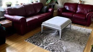 A living room with two red leather sofas, a white coffee table, and a patterned rug. - Charming 2 bedroom home.🏔 (Cranbrook)