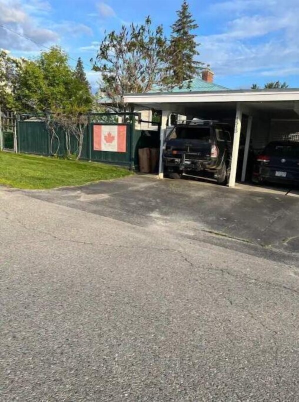 A parking garage with a covered entrance, a black vehicle inside, and a Canadian flag on a fence.