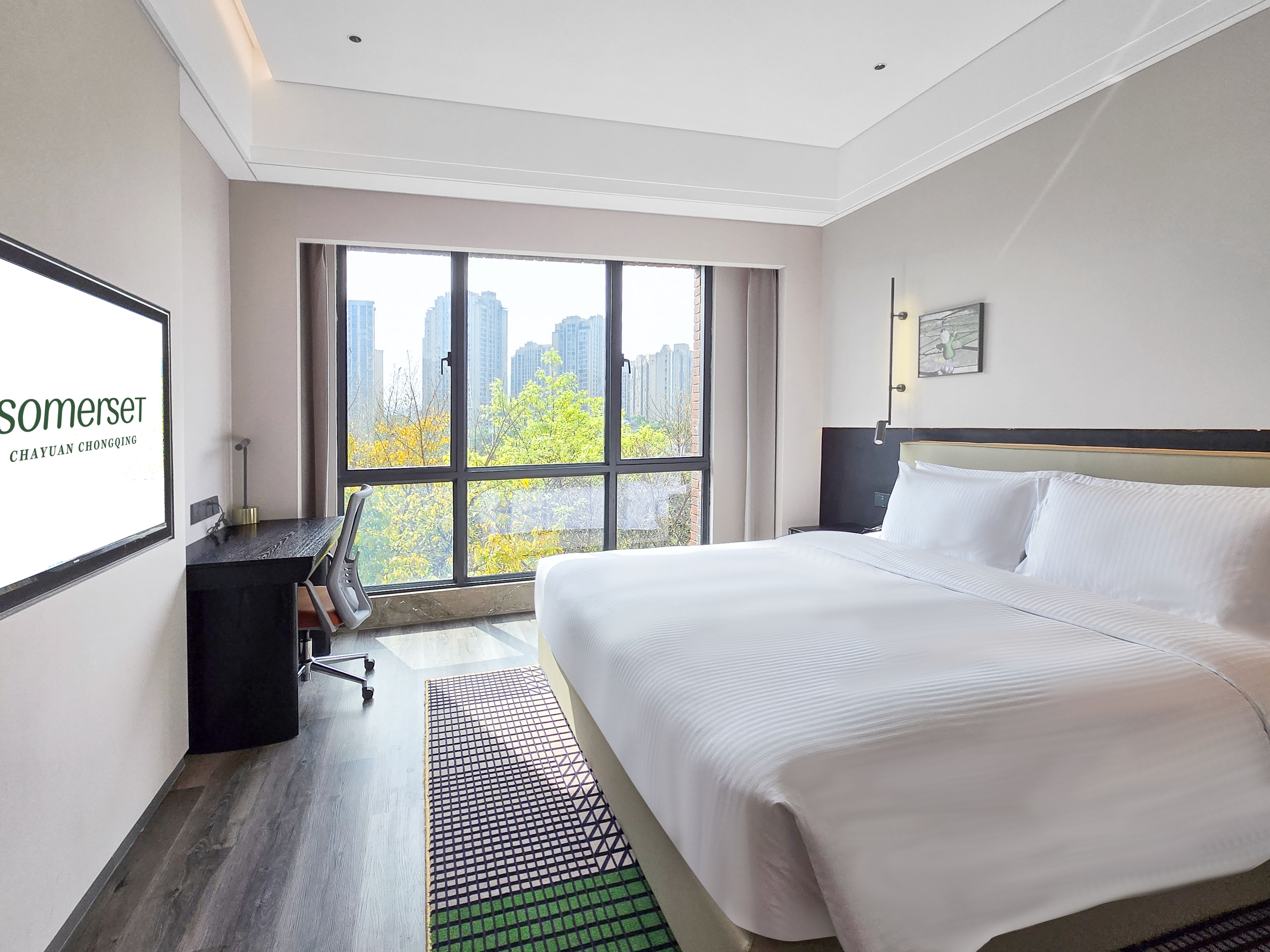A hotel room with a large bed, a desk, and a view of the cityscape through the window.