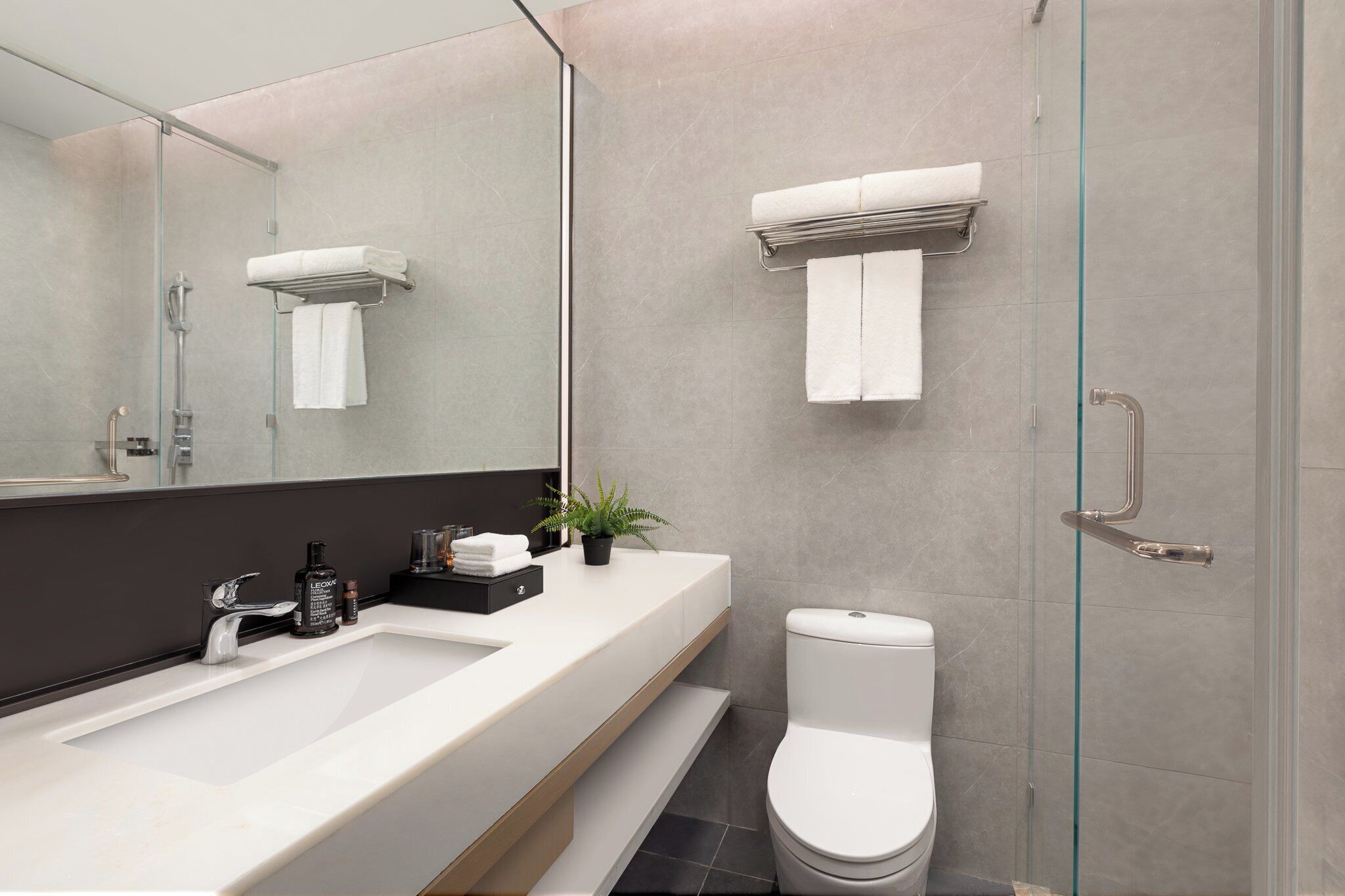 Un baño moderno con un espejo grande, un lavabo blanco, un inodoro y una cabina de ducha con paredes de vidrio.