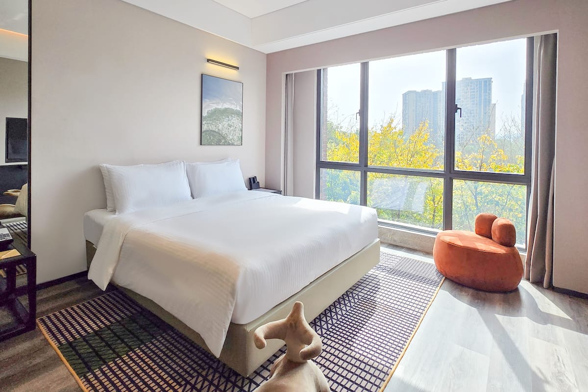 Een moderne hotelkamer met een groot bed, een bureau, een stoel en uitzicht op de skyline.