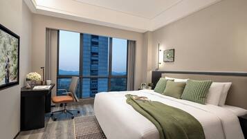 Habitación de hotel con una cama grande, un escritorio y vistas de la ciudad a través de amplias ventanas.