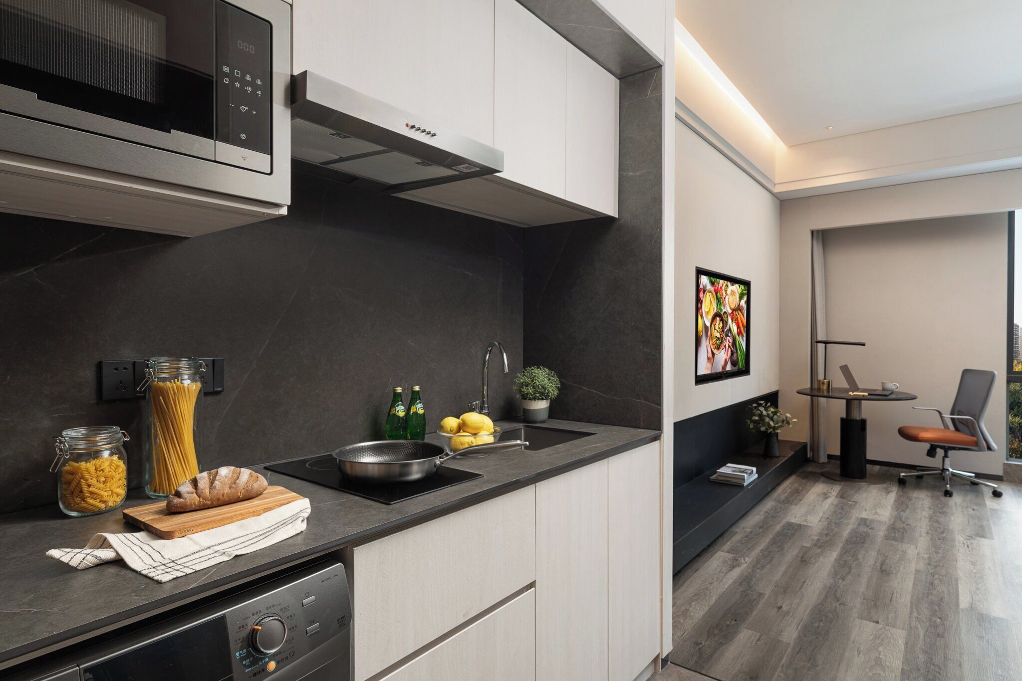 Une cuisine moderne équipée d’un four à micro-ondes encastré, d’une cuisinière et d’un évier. On peut voir des bocaux de pâtes et des citrons sur le plan de travail, et une plante accrochée au mur.