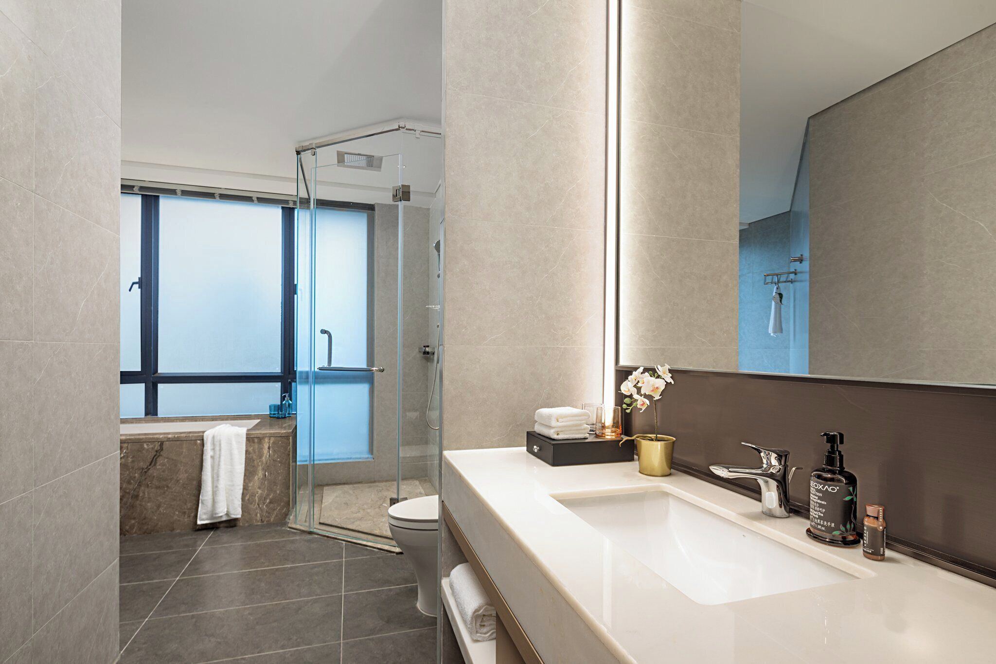 A modern bathroom with a large mirror, a shower, and a vanity with toiletries.