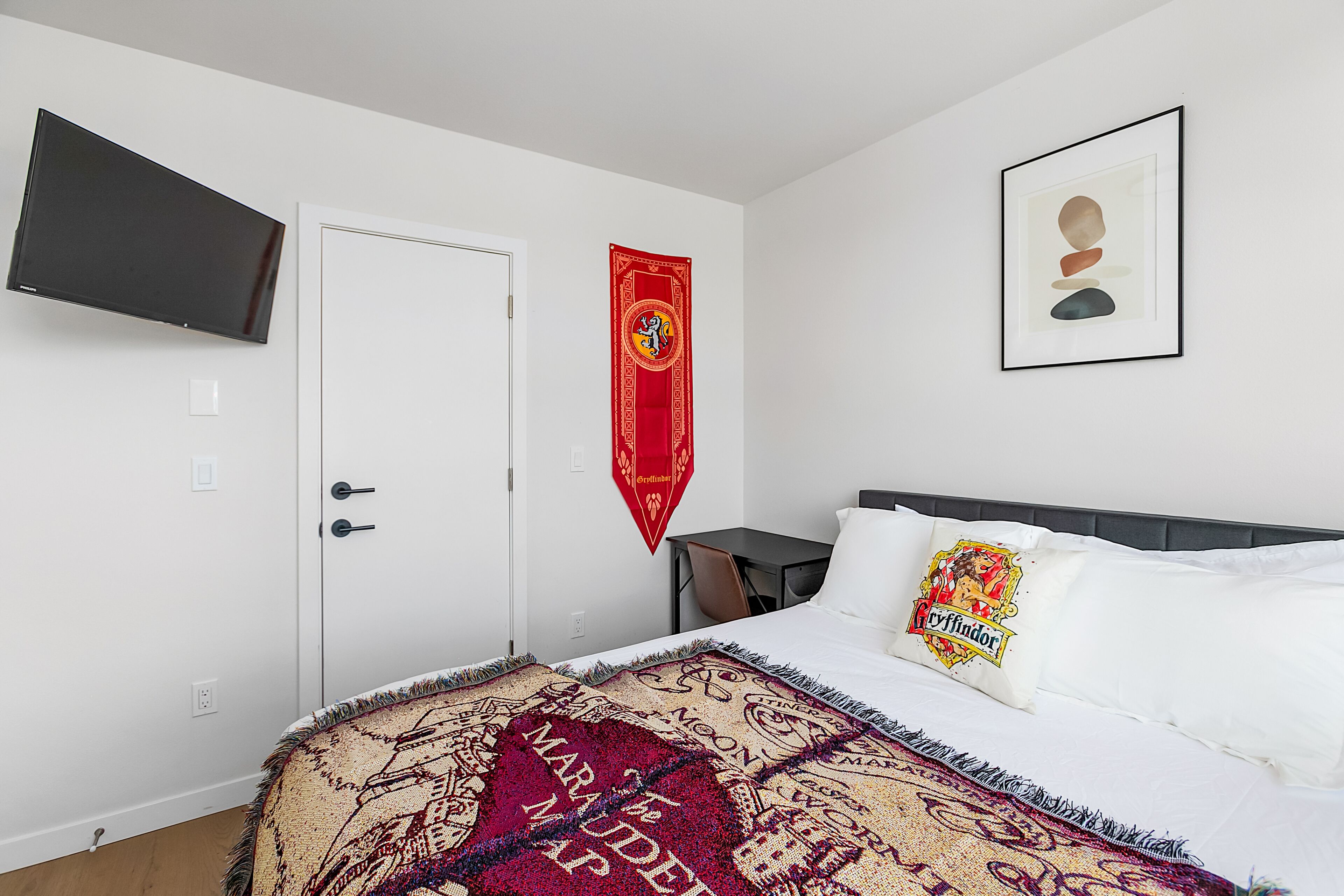 A bedroom with a bed, a TV mounted on the wall, a door, and a desk.