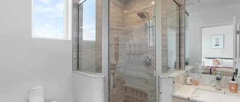 A modern bathroom with a glass-enclosed shower, a toilet, and a vanity with toiletries.