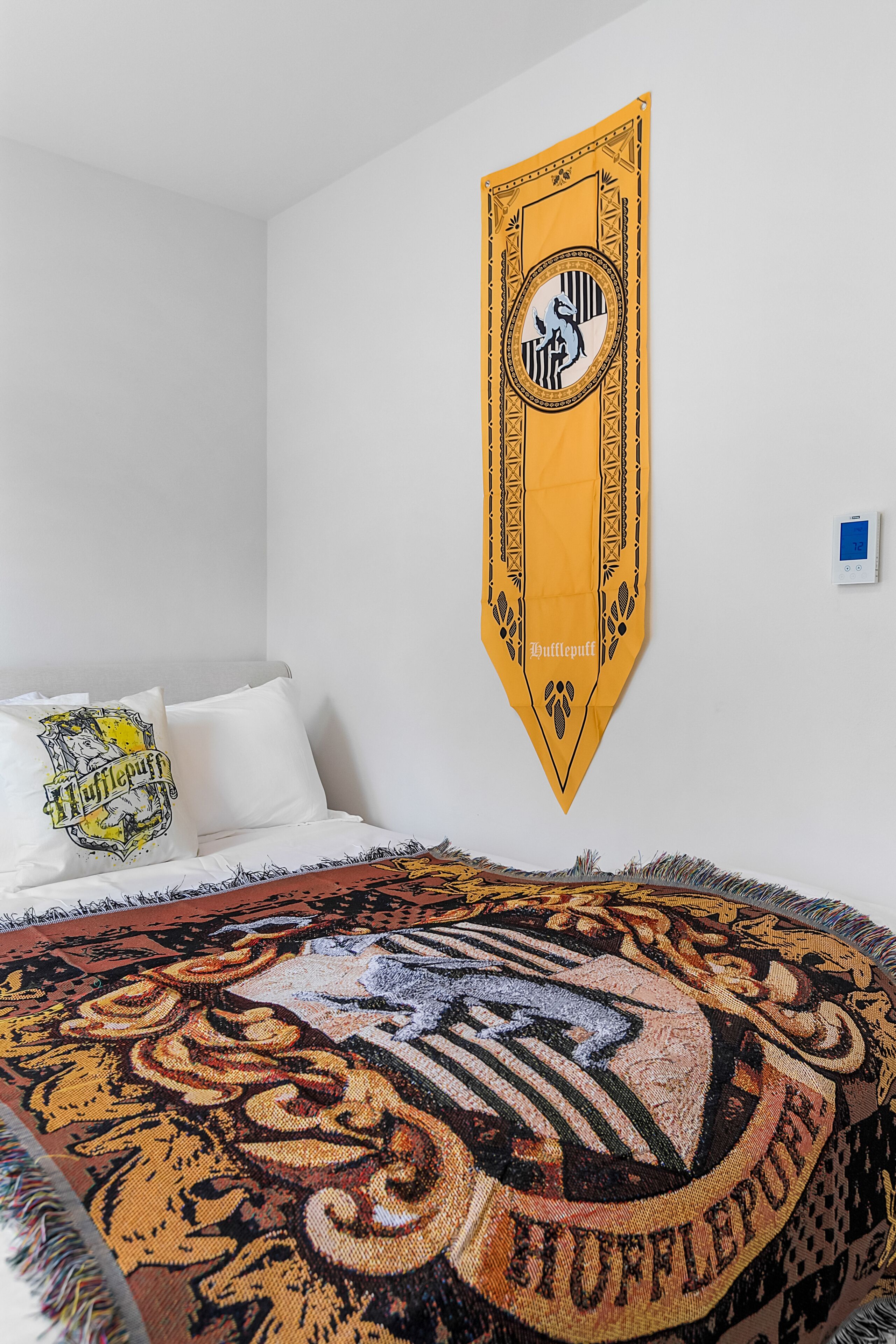 A bedroom with a large bed, a wall-mounted Hogwarts banner, and a patterned throw blanket.