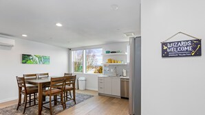 A modern kitchen with a dining area, a sign reading "WIZARDS WELCOME (MUGGLES TOLERATED)", and a window with a view of trees. - Harry Potter Sweet Suites (Seattle)