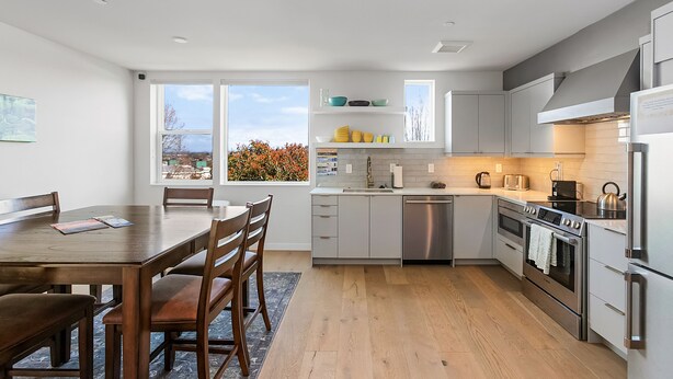 A modern kitchen with a dining area, stainless steel appliances, and a view of autumn foliage. - Harry Potter Sweet Suites (Seattle)