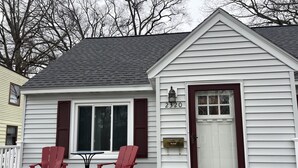 A white house with a dark brown door, a mailbox, and two red chairs on the porch. - Off season weekly and monthly rates! 700 weekly, 2400 monthly (Muskegon)