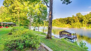 A lakeside cabin with a dock, surrounded by lush greenery and trees.