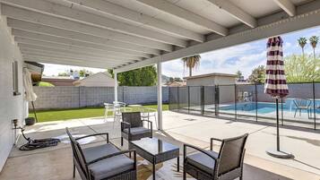 Une terrasse couverte avec des meubles d’extérieur, une piscine et une vue sur le jardin arrière.