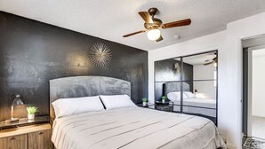 A modern bedroom with a large bed, a ceiling fan, a wall clock, and a mirror. - Cozy on Cactus, Phoenix Escape! Private Pool Oasis, Pet-Friendly, Near Top Attractions! (Phoenix)