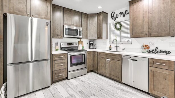 A modern kitchen with stainless steel appliances, wooden cabinets, and a 'home' sign on the wall. - Cozy on Cactus, Phoenix Escape! Private Pool Oasis, Pet-Friendly, Near Top Attractions! (Phoenix)