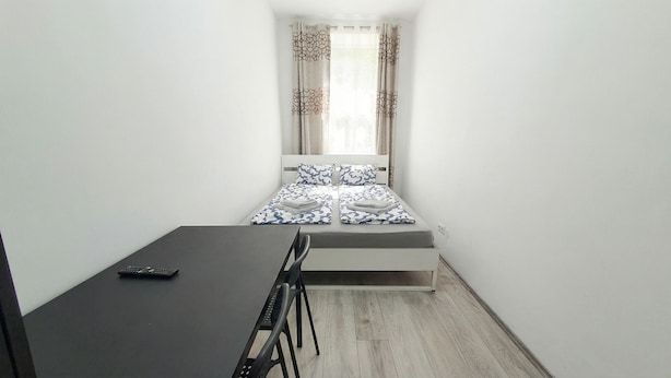 A small, narrow room with a bed at the end, a desk with a chair, and a window with curtains. - Quick Access to Vienna Center - Simple Private Rooms with WIFI (Vienna)