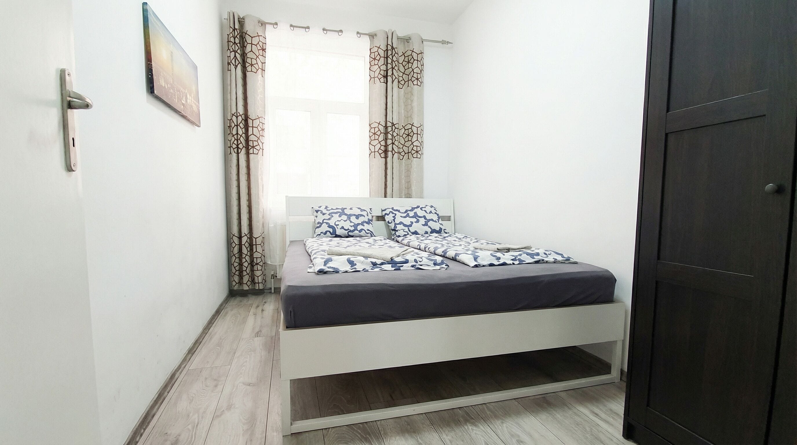Un dormitorio con cama, cortinas, una puerta y un cuadro en la pared.