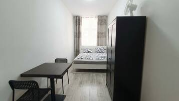 Una habitación pequeña y estrecha con una cama, una mesa, dos sillas y un armario.